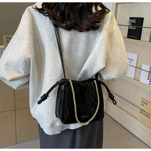 Detail of black wrinkled bucket bag with gold chain strap and drawstring design
