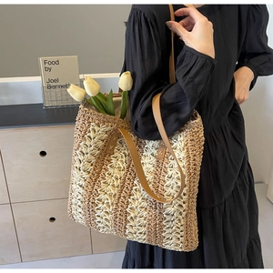 Détail d'un sac cabas en paille tissée avec anses en cuir marron porté à l'épaule
