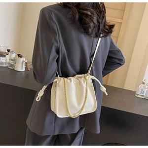 Detail of a minimalist off-white drawstring bucket bag with gold chain and crossbody strap