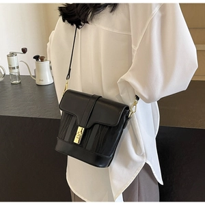 Detail of a chic black textured bucket bag with gold clasp shown on a model
