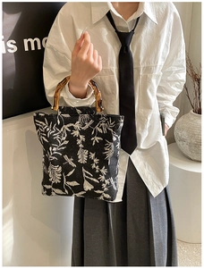 Détail d'un sac en toile noire florale avec poignée en bambou porté par un mannequin