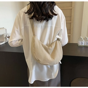 Gros plan d'un sac bandoulière croissant en nylon beige porté par un mannequin