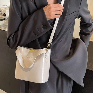 Sac seau crème brillant avec détails dorés porté sur une veste anthracite