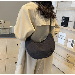 Vue de mannequin du sac bandoulière demi-lune en nylon noir porté avec un trench-coat kaki