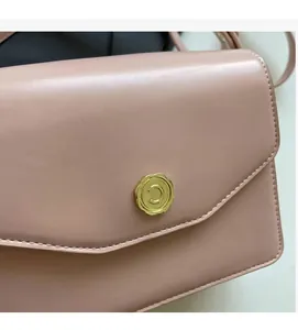 Detail of a pink crossbody bag featuring a golden wave-edged buckle with a C-letter engraving