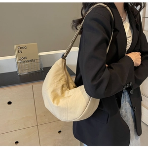 Vue détaillée d'un sac bandoulière croissant beige en nylon porté sur un blazer noir