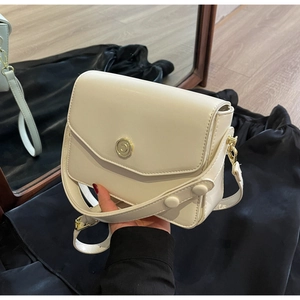 Detail of a creamy white small crossbody bag with a round gold buckle and a top handle