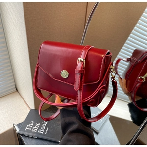 Close-up of wine red leather handbag with gold circular buckle and adjustable strap