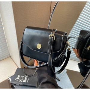 Detail of a black leather square crossbody bag featuring a gold round embossed metal buckle