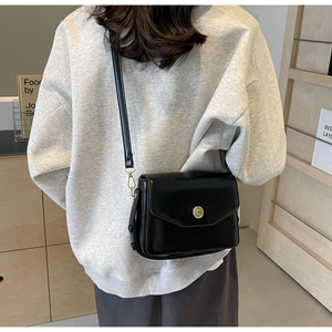 Detail of black crossbody bag featuring a golden circular clasp with C engraving
