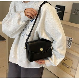 Close-up of a black leather crossbody bag with a golden rose-shaped metal magnetic clasp
