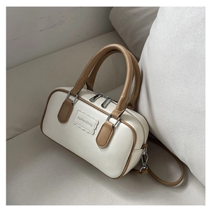 Detail of a cream Boston bag with tan trim, handle, and a stylish Fashion & bag emblem