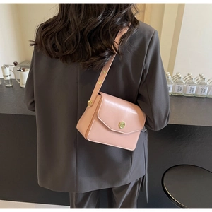 Pale pink leather shoulder bag worn over a grey blazer showing adjustable gold buckle
