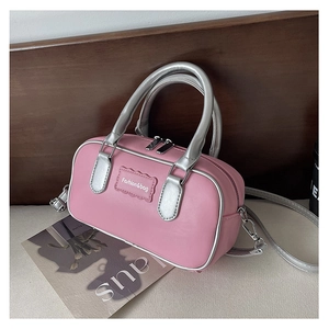Detail of pink faux leather crossbody bag with silver cylindrical handles and metal hardware
