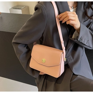 Pink leather crossbody bag detail with circular gold clasp and long shoulder strap on model