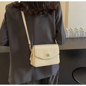 Modern off-white crossbody bag with gold buckle shown on a model for scale and style