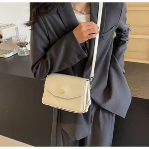 Detail of minimalist cream crossbody bag with gold round metal lock on a model