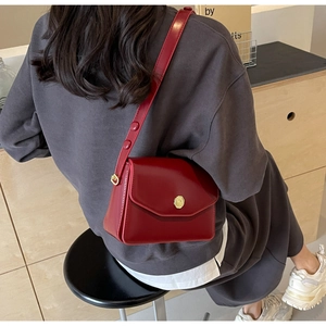 Detail view of red glossy leather shoulder bag with a gold metal oval buckle fastener