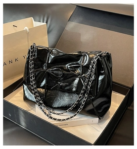 Détail du sac cabas plissé noir brillant avec chaînes et nœuds dans son coffret cadeau chic