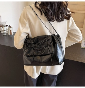 Détail du sac cabas en cuir ciré noir avec décoration de nœud et bandoulière en chaîne