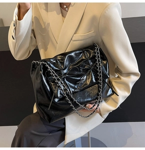Gros plan d'un sac cabas en cuir brillant noir avec nœud cousu et chaîne argentée