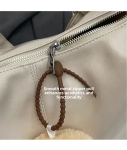 Detail eines silbernen Reißverschlusses mit braunem Anhänger an einer beigen Tasche