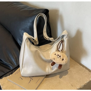Detail der cremefarbenen matten Ledertasche mit süßem braunem Plüschkeks-Anhänger und Reißverschluss