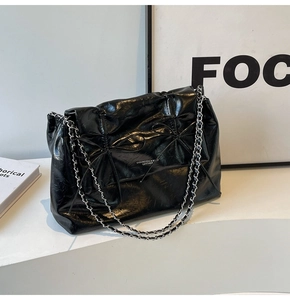 Détail du sac cabas en cuir froissé noir brillant avec doubles chaînes et nœuds décoratifs