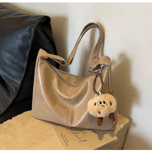Detailansicht der khakifarbenen Ledertasche mit modischer Faltenoptik und Plüsch-Anhänger