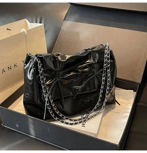 Détail d'un cabas en cuir verni noir brillant avec nœuds chics et bandoulière chaîne