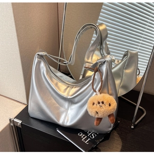 Detail der silbernen Metallic-Hobo-Tasche mit süßem Plüsch-Keks-Anhänger auf einem Tisch