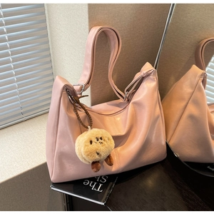 Detailaufnahme einer rosa PU-Leder-Einkaufstasche mit einem Plüschanhänger auf Büchern