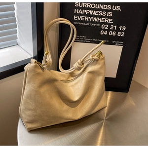 Detail of beige tote bag showing knotted shoulder strap and gold metal hardware accents
