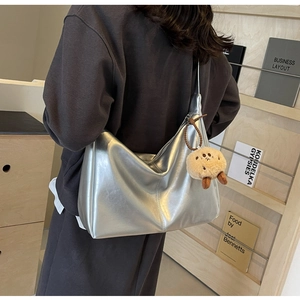 Detail der silbernen Metallic-Hobo-Tasche mit Plüsch-Anhänger und glatter PU-Leder-Textur