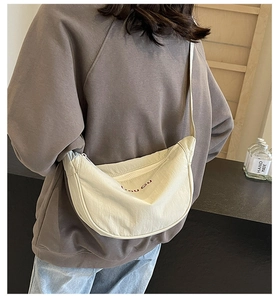 Close-up of off-white canvas crescent bag with red embroidery and zip closure