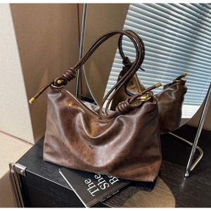 Detail of dark brown leather tote bag with knotted strap and gold metallic hardware