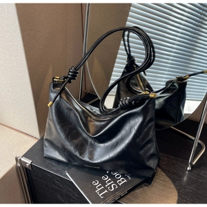 Detail of black leather tote bag featuring gold knotted metal hardware and smooth texture
