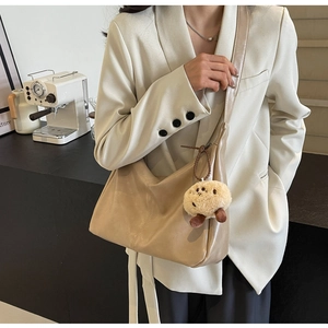 Detailansicht der minimalistischen beigen Hobo-Tasche mit breitem Gurt und Bärenanhänger