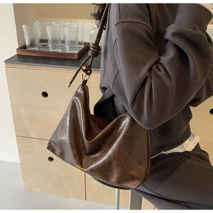 Detail of dark brown leather tote with knot strap and golden cylindrical hardware