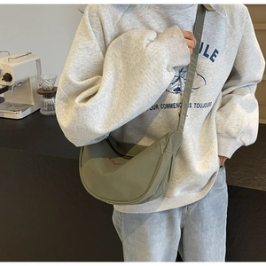 Olive green nylon crescent bag with red embroidery detail worn in a cozy cafe setting