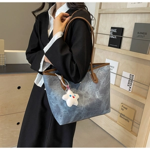 Détail d'un grand sac cabas en denim bleu avec anses en cuir porté par un mannequin