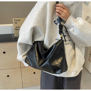 Detail of black leather tote bag featuring a knotted strap design and gold hardware
