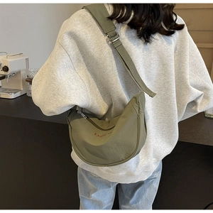 Olive green nylon crescent bag shown on model in a casual lifestyle cafe setting