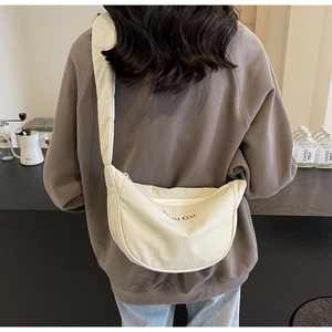 Detail of off-white nylon crescent crossbody bag with red embroidery on a cafe background