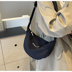 Close-up of black nylon crescent bag with Dou lettering shown on model's shoulder