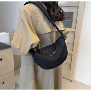 Detail of black nylon half-moon crossbody bag with white Dou Gu logo on beige coat