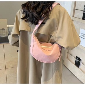 Detail of pink nylon half-moon crossbody bag with Dou Gu logo worn over a trench coat