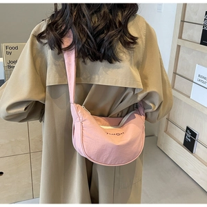 Pink nylon crescent crossbody bag with shoulder strap worn over a beige trench coat