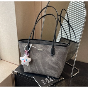 Détail du cabas gris texturé avec plaque logo argentée et charm étoile en peluche blanche