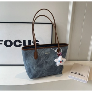 Détail du cabas en denim bleu avec garniture en cuir marron et pendentif étoile en peluche